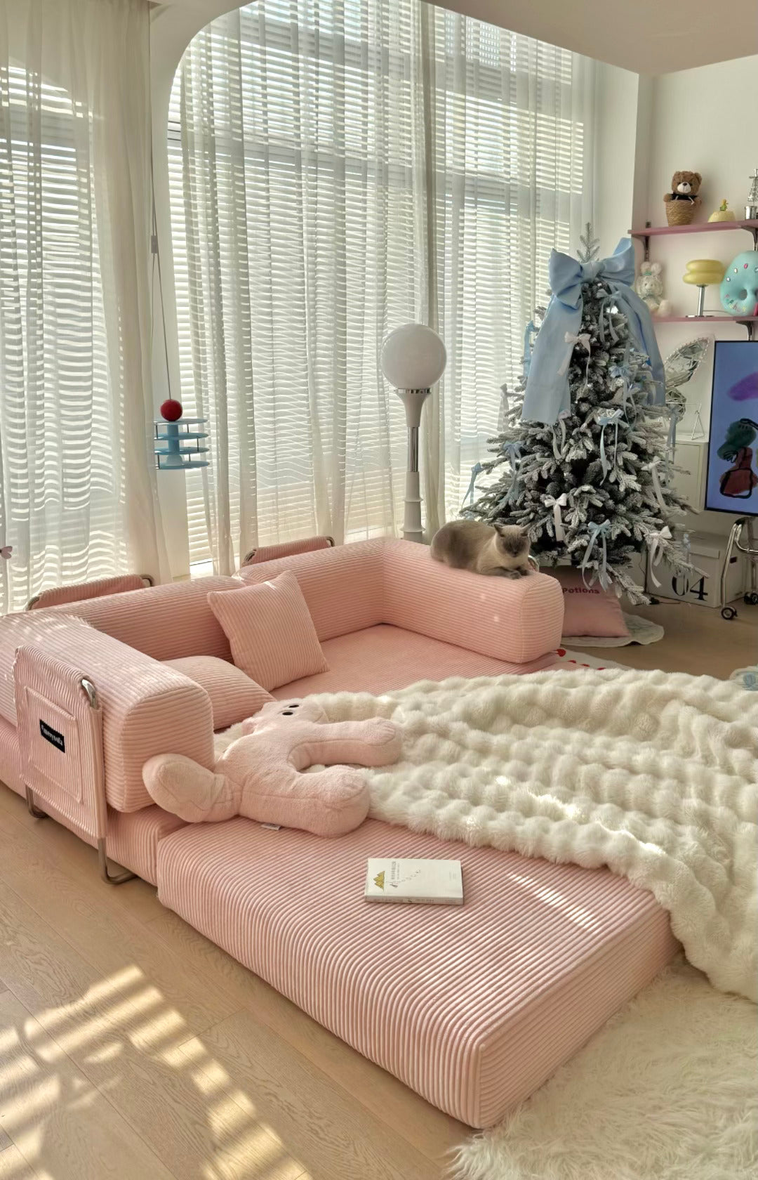 Pink sectional sofa in a living room with a decorated Christmas tree and soft lighting.